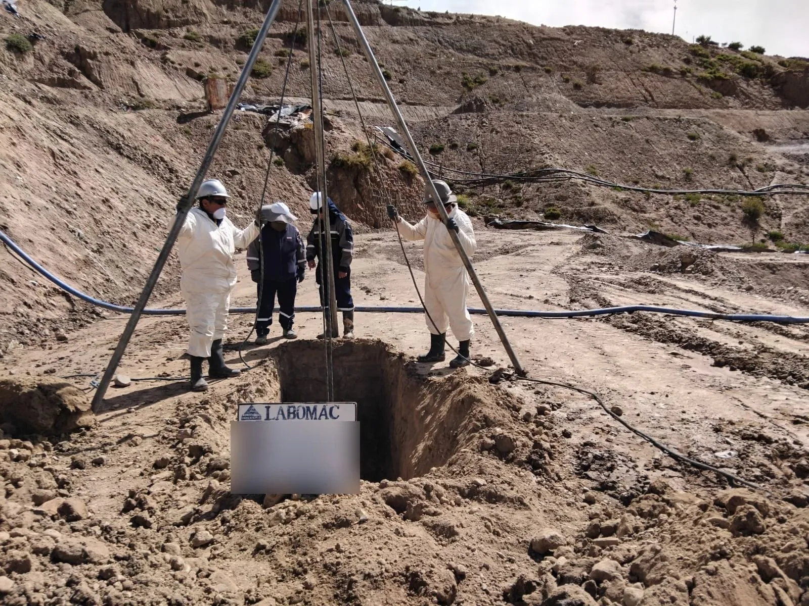 Cuatro técnicos con equipo de protección junto a un pozo de exploración con trípode, en terreno abierto.